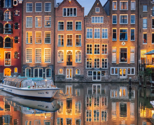 typische krumme und schmale Haeuser in Amsterdam spiegeln sich im Wasser buchbar bei Olivers Touristik World