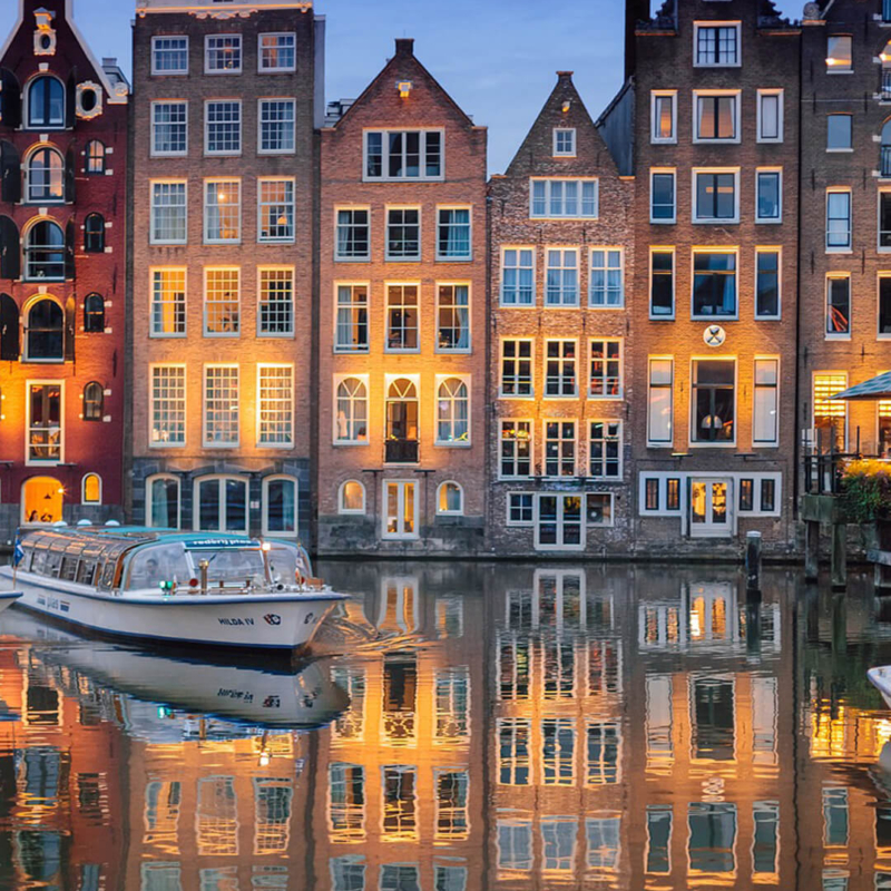 typische krumme und schmale Haeuser in Amsterdam spiegeln sich im Wasser buchbar bei Olivers Touristik World