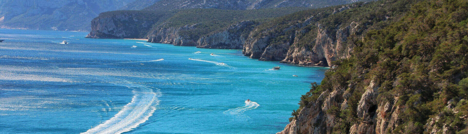 Blick-auf-die-Steikueste-von-Sardinien-in-Italien Blick auf die Steilküste von Sardinen mit Booten im blauen Meer